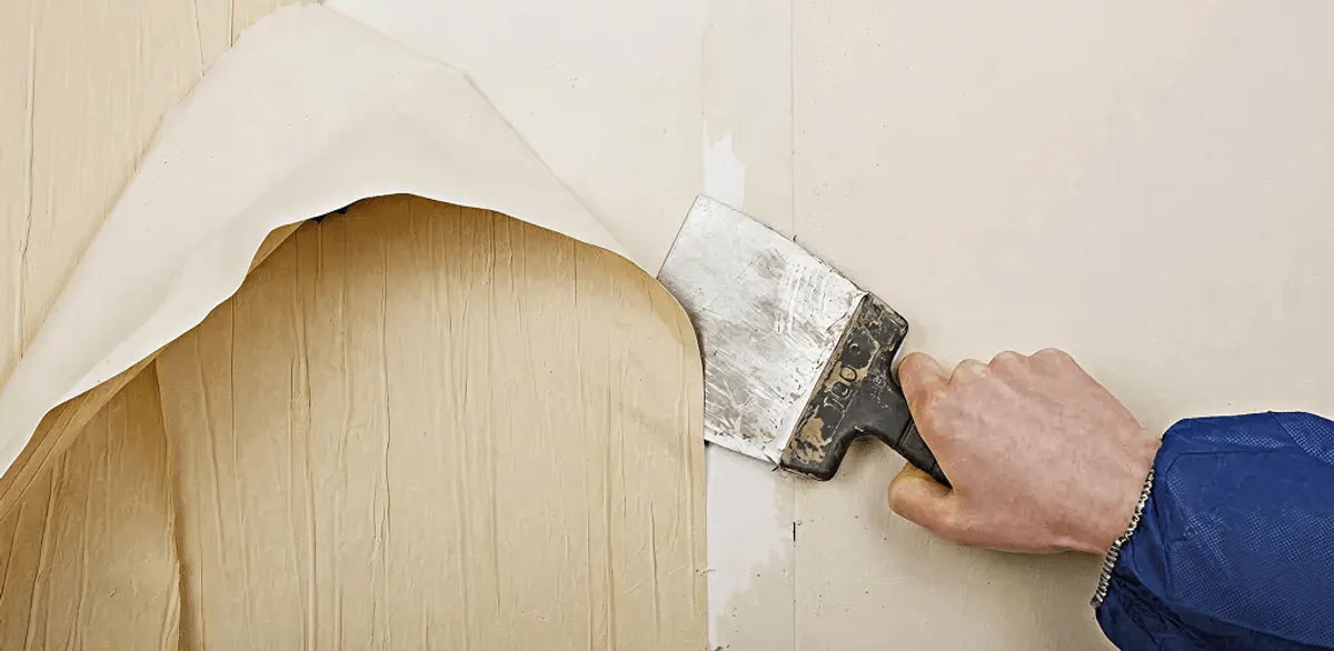 Handyman removing wallpaper with a scraper for wall preparation in Manchester, NH