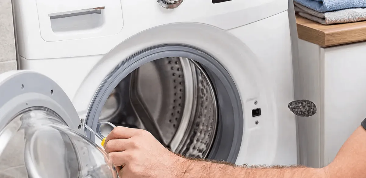 Handyman repairing a front-load washing machine and inspecting the drum in Manchester, NH