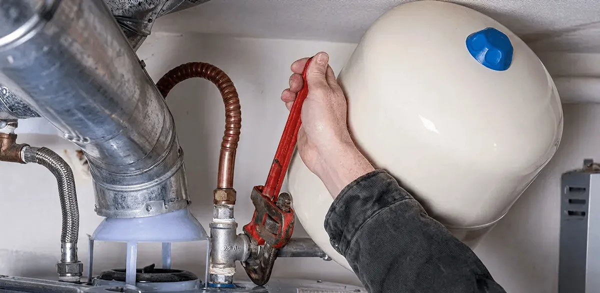 Water heater repair technician tightening plumbing connections near a tank unit in Manchester, NH